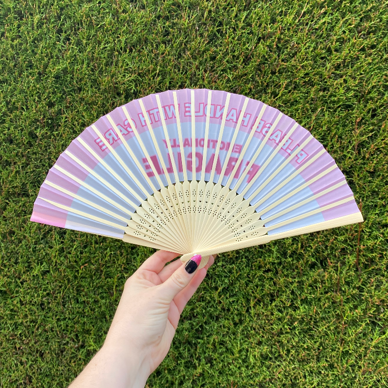 Handheld Fan with pink and white lettering reading "Please handle with care, Emotionally Fragile" with natural Bamboo Spines