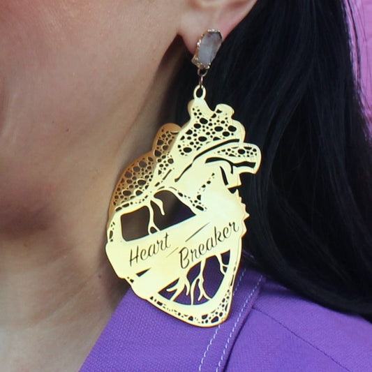 18K Gold Statement Earrings shaped as an anatomical heart with a banner wrapped around the middle reading "Heart Breaker" featuring Clear Quartz rough cut crystals.