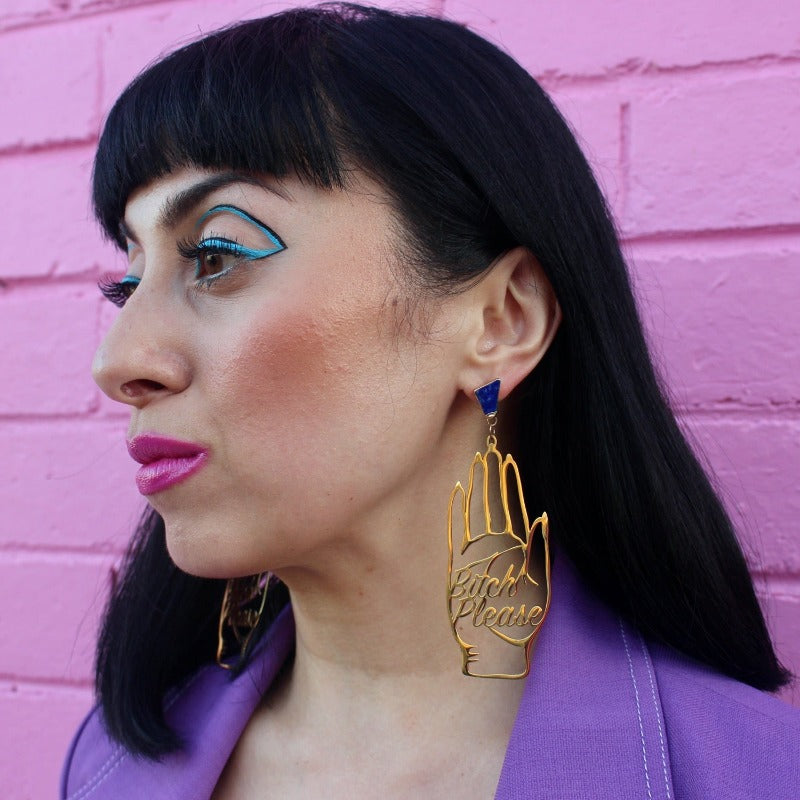 18K Gold Statement Earrings shaped as a hand and reading "Bitch Please" featuring Lapis Lazuli rough cut crystals modelled by Margeaux in front of a pink brick wall