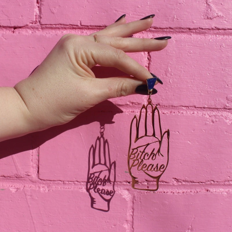 18K Gold Statement Earrings shaped as a hand and reading "Bitch Please" featuring Lapis Lazuli rough cut crystals held in front of a pink brick wall