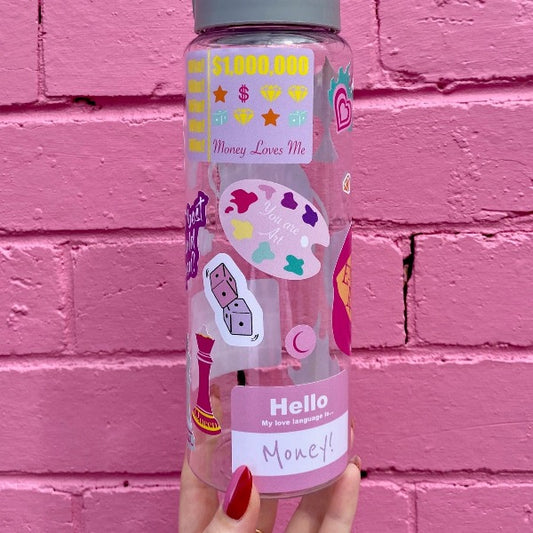 Two bold coloured fun sticker on a water bottle held up in front of a pink brick wall. Featuring stickers such as Eat the Rich, Just like Magic, You are Art.