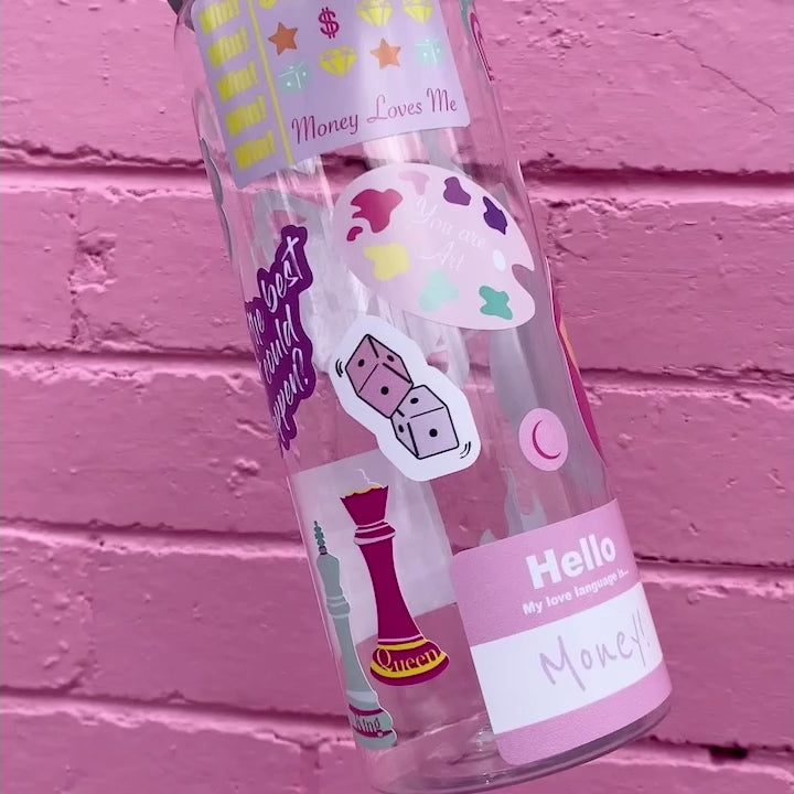 Two bold coloured fun sticker on a water bottle held up in front of a pink brick wall. Featuring stickers such as Eat the Rich, Just like Magic, You are Art.